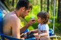 Young father feeds his daughter seeds on vacation in woods.