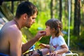 Young father feeds his daughter seeds on vacation in woods.