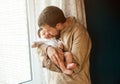 Young father gently holding and kissing his baby near the window at home Royalty Free Stock Photo