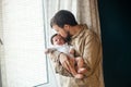 Young father gently holding and kissing his baby near the window at home Royalty Free Stock Photo