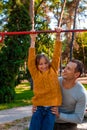 Father helping daughter to pull up on the uneven bars at the playground. Healthy family concept