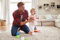 Young father helping toddler daughter walk in sitting room