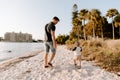 Young Father and His Cute Little Boy Son Walking and Enjoying the Nice Outdoor Weather on the Sandy Beach next to the Ocean Bay