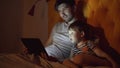 Young father and his little son watching cartoon movie using tablet computer while lying in bed in evening at home Royalty Free Stock Photo