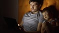 Young father and his little son watching cartoon movie using tablet computer and talking while lying in bed in evening Royalty Free Stock Photo