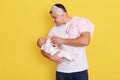 Young father holding and feeding her baby isolated over yellow background, handsome young dad looking at her infant baby with Royalty Free Stock Photo