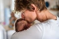 A young father holding a newborn baby at home, kissing him.