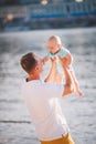 A young father holds one year of his son in his arms with a smile and loves hugs and throws him on the river bank on the beach Royalty Free Stock Photo