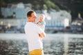 A young father holds one year of his son in his arms with a smile and loves hugs and throws him on the river bank on the beach Royalty Free Stock Photo