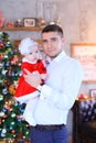 Young father keeping little daughter near Christmas tree in background.