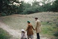 Young father, mother and little toddler daughter girl in a beret and a coat walk holding hands in the autumn forest Royalty Free Stock Photo