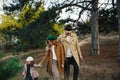 Young father, mother and little toddler daughter girl in a beret and a coat walk holding hands in the autumn forest. Royalty Free Stock Photo