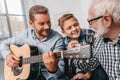Young father playing guitar while little son and grandfather are
