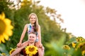 A young father plays with his daughter in a field of sunflowers. A little girl sits on her father`s neck and laughs. Family summer