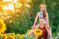 A young father plays with his daughter in a field of sunflowers. A little girl sits on her father`s neck and laughs. Family summer