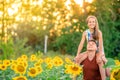 A young father plays with his daughter in a field of sunflowers. A little girl sits on her father`s neck and laughs. Family summer