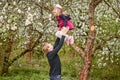 A young father plays with his daughter in a flowering garden. Throws up. Against the background of green grass and flowering trees
