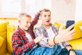 Young father with a son, a boy of 8 years old in checkered shirts, sitting on a yellow sofa, taking a selfie on a mobile phone,