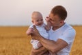 Young father tenderly holding cute baby in his arms. Background of ripe wheat field. Portrait of dad and small child Royalty Free Stock Photo