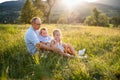 Young father with two small children sitting on meadow outdoors at sunset. Royalty Free Stock Photo