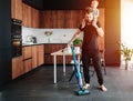 Young father vacuums apartment floor with his baby riding on his neck