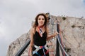 A young fearless woman in safety gear walks over a rope bridge over a precipice high in the mountains.