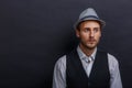 A young fellow in a hat and vest, looking away with a calm look.