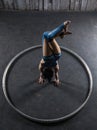 Young female acrobat standing on hand inside big metal hoop