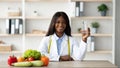 Young female african american nutritionist holding glass of water while sitting at table with fruits and vegetables Royalty Free Stock Photo