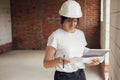 Young female architect with tablet checking blueprints against of building new modern house. Stylish happy woman engineer in hard Royalty Free Stock Photo