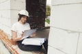 Young female architect with tablet checking blueprints while sitting in window of new modern house. Stylish woman engineer in hard Royalty Free Stock Photo