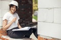 Young female architect with tablet checking blueprints while sitting in window of new modern house. Stylish woman engineer in hard Royalty Free Stock Photo