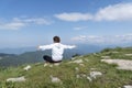 Young female with arms outstretched is sitting on top of mountain peak with sense of freedom.