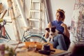 A young female artist is playing with her dog while making a break from a work on a new painting in the studio. Art, painting, Royalty Free Stock Photo