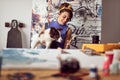 A young female artist is playing with her dog while working on a new painting in the studio. Art, painting, friendship, studio Royalty Free Stock Photo