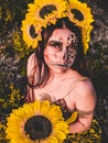 Young female with artistic spooky makeup and sunflower on head posing at the camera in a field