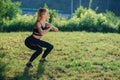 Young female athlete doing squat exercises outdoors in park. Fit girl working out her core and glutes with bodyweight.