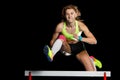 Young female athlete jumping over hurdle in sprint