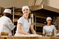 young female baker kneading dough at baking manufacture while her colleagues working blurred