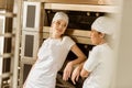 young female bakers leaning on industrial oven at baking manufacture