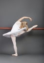 Young female ballet dancer stretching at ballet bar over grey background Royalty Free Stock Photo