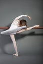 Young female ballet dancer stretching at ballet bar over grey background Royalty Free Stock Photo