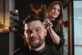 Young female barber portrait evaluates her hairstyle work for smiling bearded man looking at mirror. Modern low light black style Royalty Free Stock Photo