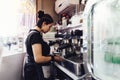 Young female barista in gloves prepares coffee. Brunette girl pours whipped milk for cocktail into paper cup Royalty Free Stock Photo