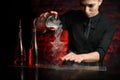 Young female barman accurate pours smoky cocktail from mixing bowl into martini glass.