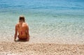 Young female in bikini sitting in shallow sea, left