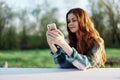 A young female blogger sits outdoors with her smartphone in hand and freelances in the outdoors. The concept of a