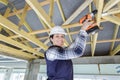 Young female builder working on wooden roof joist