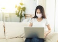 Young female businesswoman staying at home, using a laptop for work on the sofa, and wearing a mask to protect herself from the Royalty Free Stock Photo