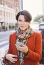 Beautiful Woman with Short Hair Looking at the Camera Smiling With Smart Phone in her Hand in the City